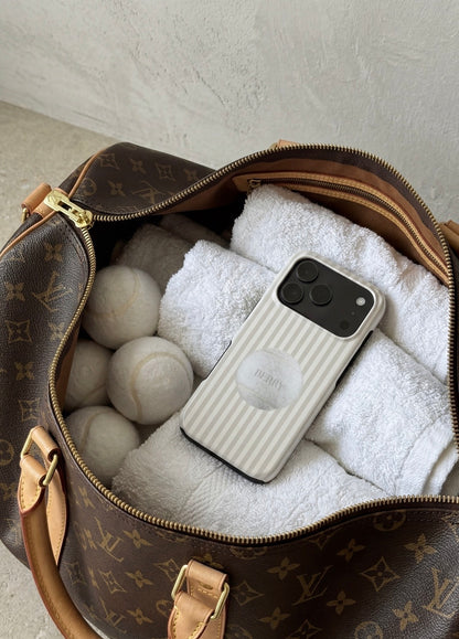 A trendy phone case with beige and white stripes featuring a stylish tennis ball design, placed on white towels inside a luxury bag.